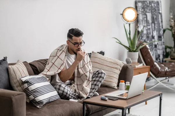 Um homem de cabelos escuros sentindo-se mal e sentado coberto com uma xadrez — Fotografia de Stock