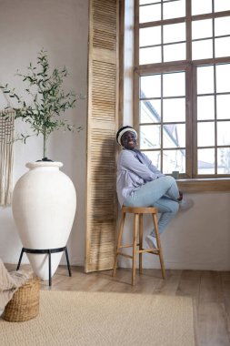 Açık renk elbiseli Afrikalı kadın evde vakit geçiriyor.