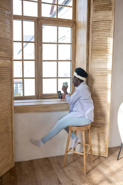 African woman with a smartphone sitting near the window — Photo