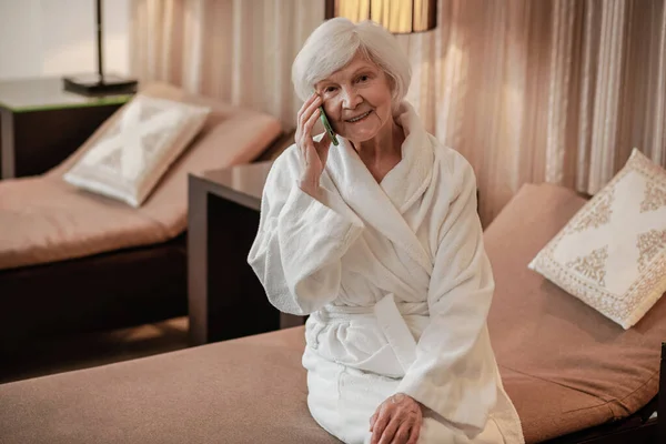 Mulher idosa bonita em roupão branco com um telefone nas mãos — Fotografia de Stock