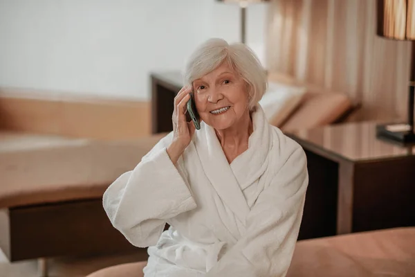 Good-looking elderly woman in white robe with a phone in hands — ストック写真
