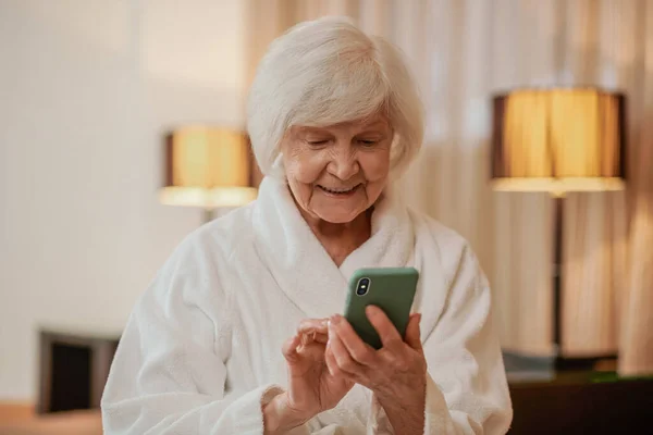 携帯電話を手に白い衣を着た格好いいお年寄り女性 — ストック写真
