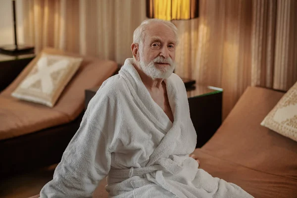 Šedovlasý vousáč v bílém rouchu v hotelovém pokoji — Stock fotografie