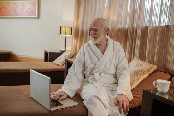 Egy ősz hajú férfi fehér köntösben néz valamit egy laptopon. — Stock Fotó