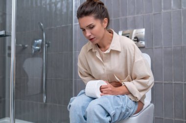 Young woman sitting on a toilet and suffering from indigestion