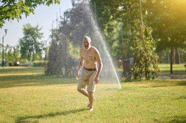 Parkta duşun altında şortlu yarı çıplak bir adam.