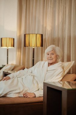 Otel odasında beyaz bornozlu, yakışıklı yaşlı bir kadın.
