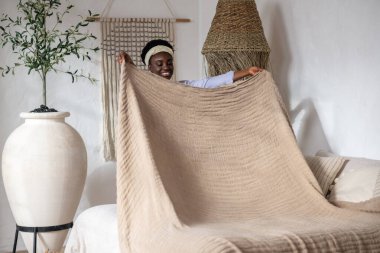 Yatak odasında yatağı yapan siyah saçlı kadın.