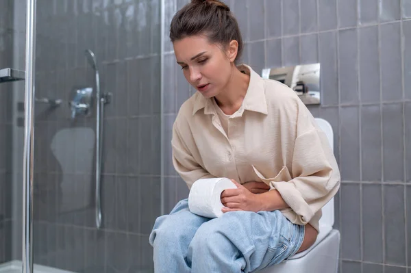 Молодая женщина сидит на унитазе и страдает от несварения желудка — стоковое фото