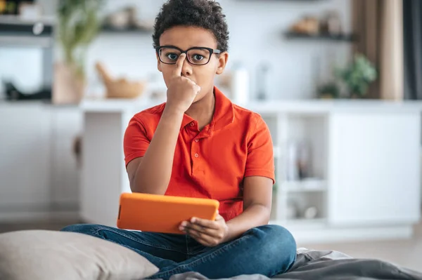 Un chico con camiseta naranja tocando sus gafas y luciendo serio —  Fotos de Stock