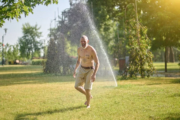 Parkta duşun altında şortlu yarı çıplak bir adam.