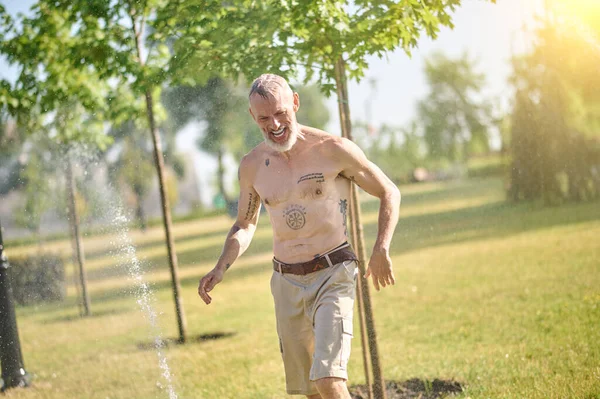 Parkta duşun altında şortlu yarı çıplak bir adam.