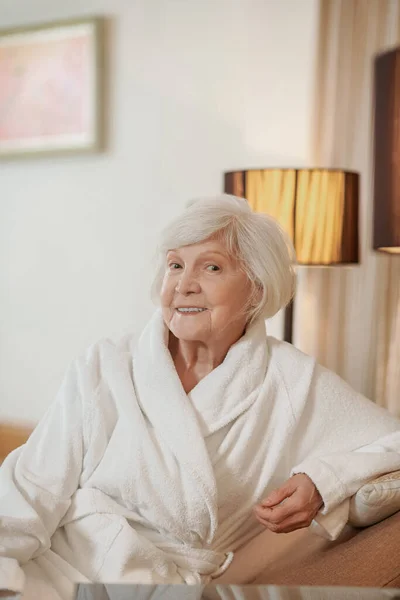 Egy csinos idős hölgy fehér köpenyben egy hotelszobában. — Stock Fotó