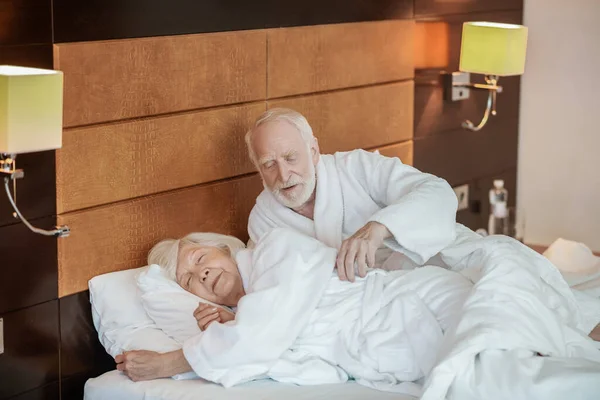 Un hombre canoso mirando con ternura a su esposa mientras ella dormía — Foto de Stock