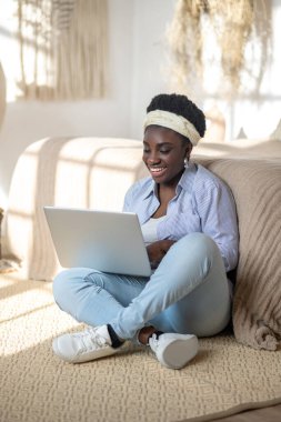 African american woman sitting on the sofa and spending time in chat online