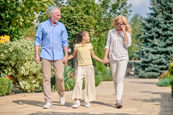 Orta yaşlı bir adam ve kadın uzun saçlı tatlı bir kızla yürüyorlar.