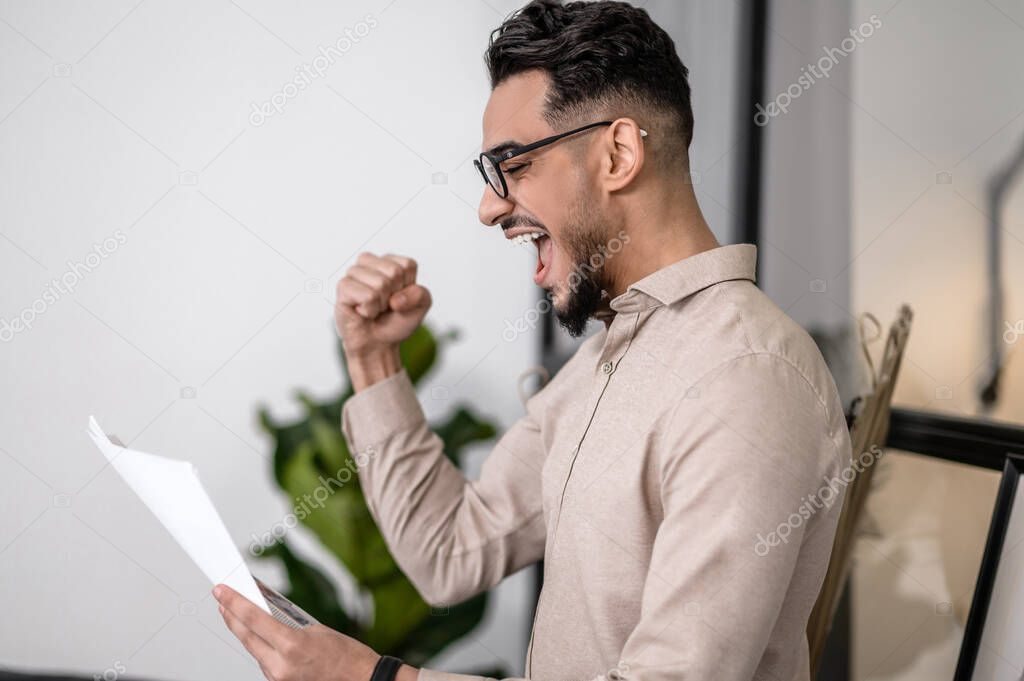A handsome young man looking excited while readng something online