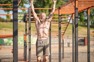 A gray-haired mature man having a workout on the open sports ground