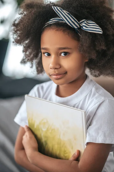 A girl sigtting on a ned with a book in hands — Stockfoto