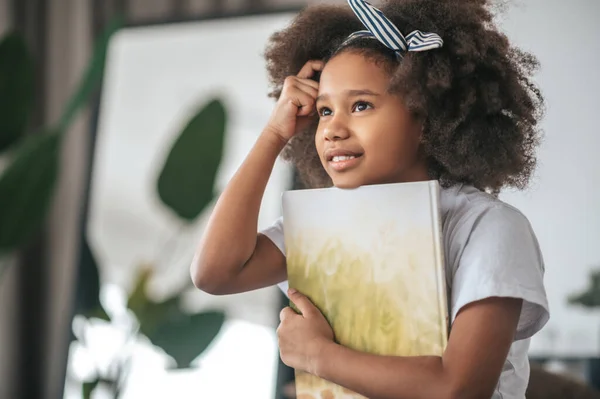 A smiling curly-haired girl with a book in hands — 스톡 사진