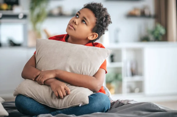 A boy with a pillow in hands looking upset — Stockfoto