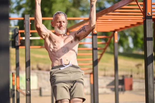 Šedovlasý dospělý muž, který cvičí na otevřeném sportovním hřišti — Stock fotografie