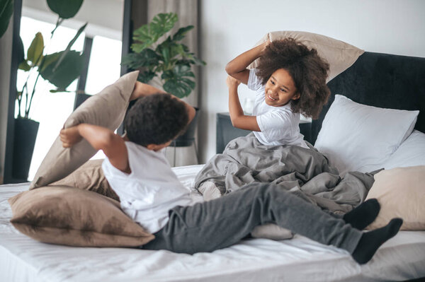 Siblings spending time at home and playing with pillows