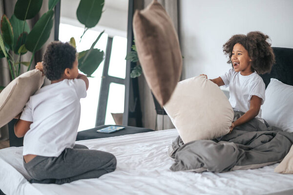 Siblings spending time at home and playing with pillows