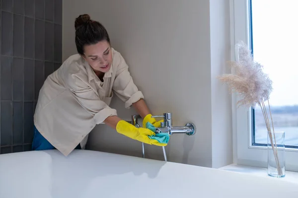 A service woman polishing faucet in the bathroom — стоковое фото