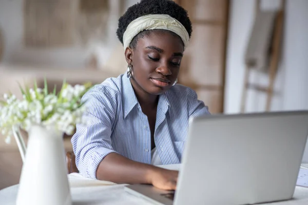 Afro-Amerikalı kadın masada oturuyor ve bir dizüstü bilgisayar üzerinde çalışıyor. — Stok fotoğraf