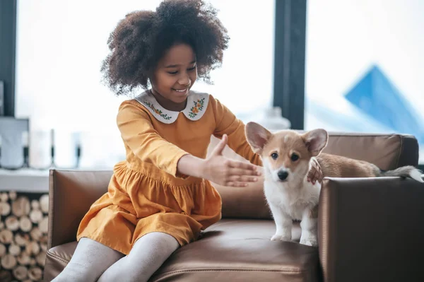 A girl in an orange dress playing with a puppy