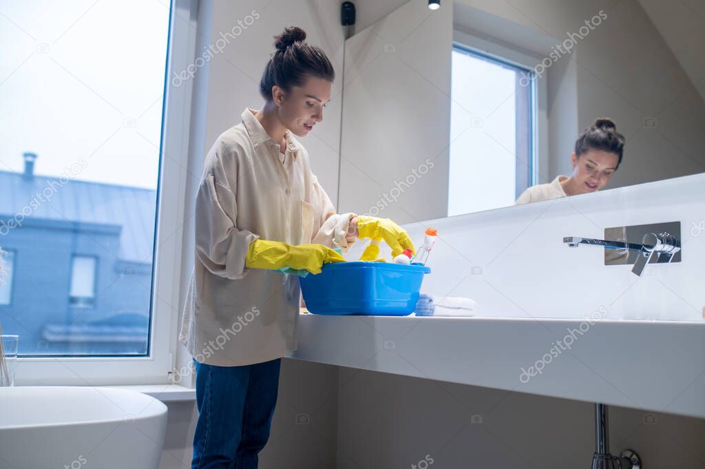 A young woman with a box with detergents in the bathroom