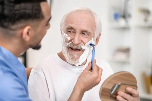 Pensioner gazing at a volunteer shaving off his stubble — Stock Photo, Image