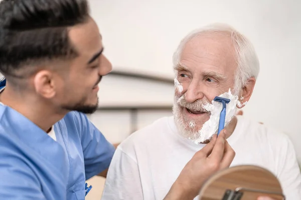 Voluntario cariñoso dando a un caballero mayor un afeitado — Foto de Stock
