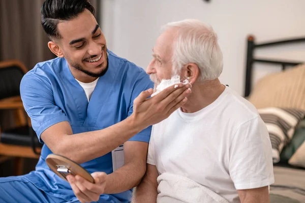 Joyful young volunteer preparing an old man for a shave —  Fotos de Stock