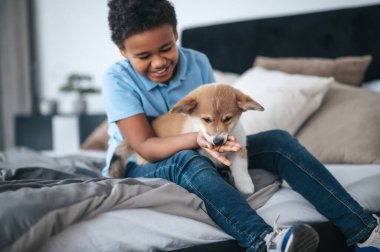 Koyu tenli bir çocuk kucağında sevimli bir köpek yavrusu ve gülümsüyor.