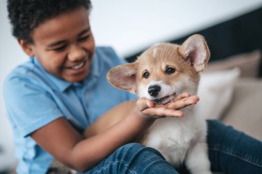 Koyu tenli bir çocuk kucağında sevimli bir köpek yavrusu ve gülümsüyor.