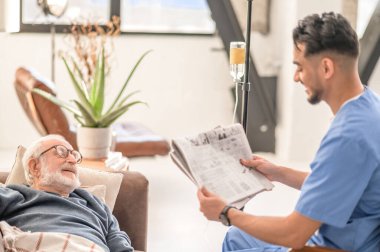 Volunteer entertaining an old man on the intravenous drip