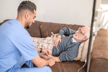 Yoğunlaşmış hemşire erkek bir hastayı damar içi tedaviye hazırlıyor.