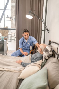 Doktor, hasta bir hastayı ev ziyareti sırasında neşelendiriyor.