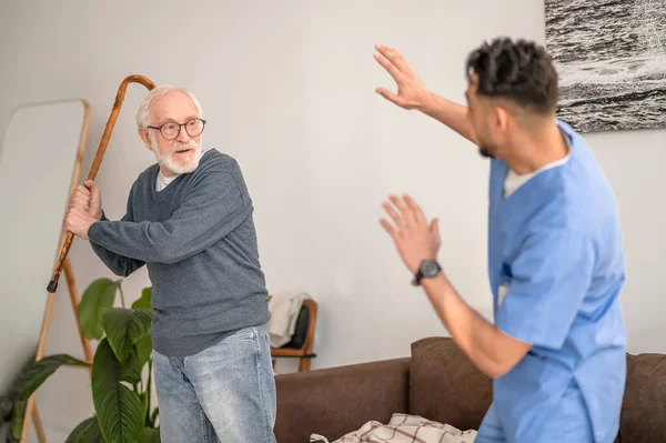 Pensionista agresivo blandiendo el bastón a su cuidador — Foto de Stock