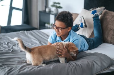 Gülümseyen çocuk bir köpek yavrusuyla oynuyor ve mutlu görünüyor.