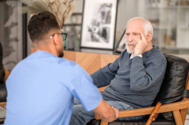 Despondent pensioner seated in the room before his caretaker