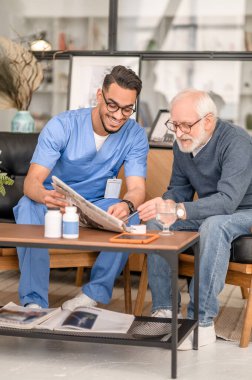 Cheerful volunteer and a focused old man reading news together