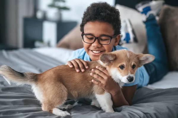 Gülümseyen çocuk bir köpek yavrusuyla oynuyor ve mutlu görünüyor.