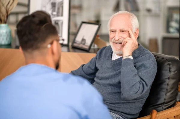 Счастливый пожилой человек разговаривает со своим домашним сиделкой — стоковое фото