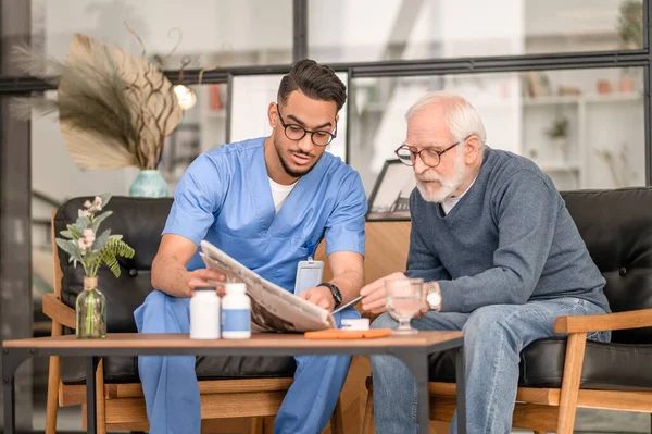 Koncentrerad äldre person och hans vårdare läsande nyheter — Stockfoto