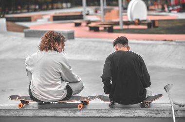 Back view of girl and guy sitting on skateboards