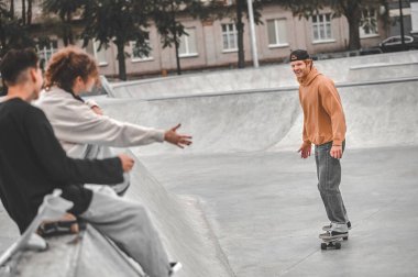 Guy on skateboard looking at friends sitting gesturing