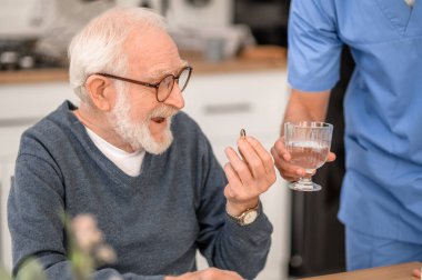 Bir tıp işçisinin gözetiminde ilaç alan yaşlı bir adam.